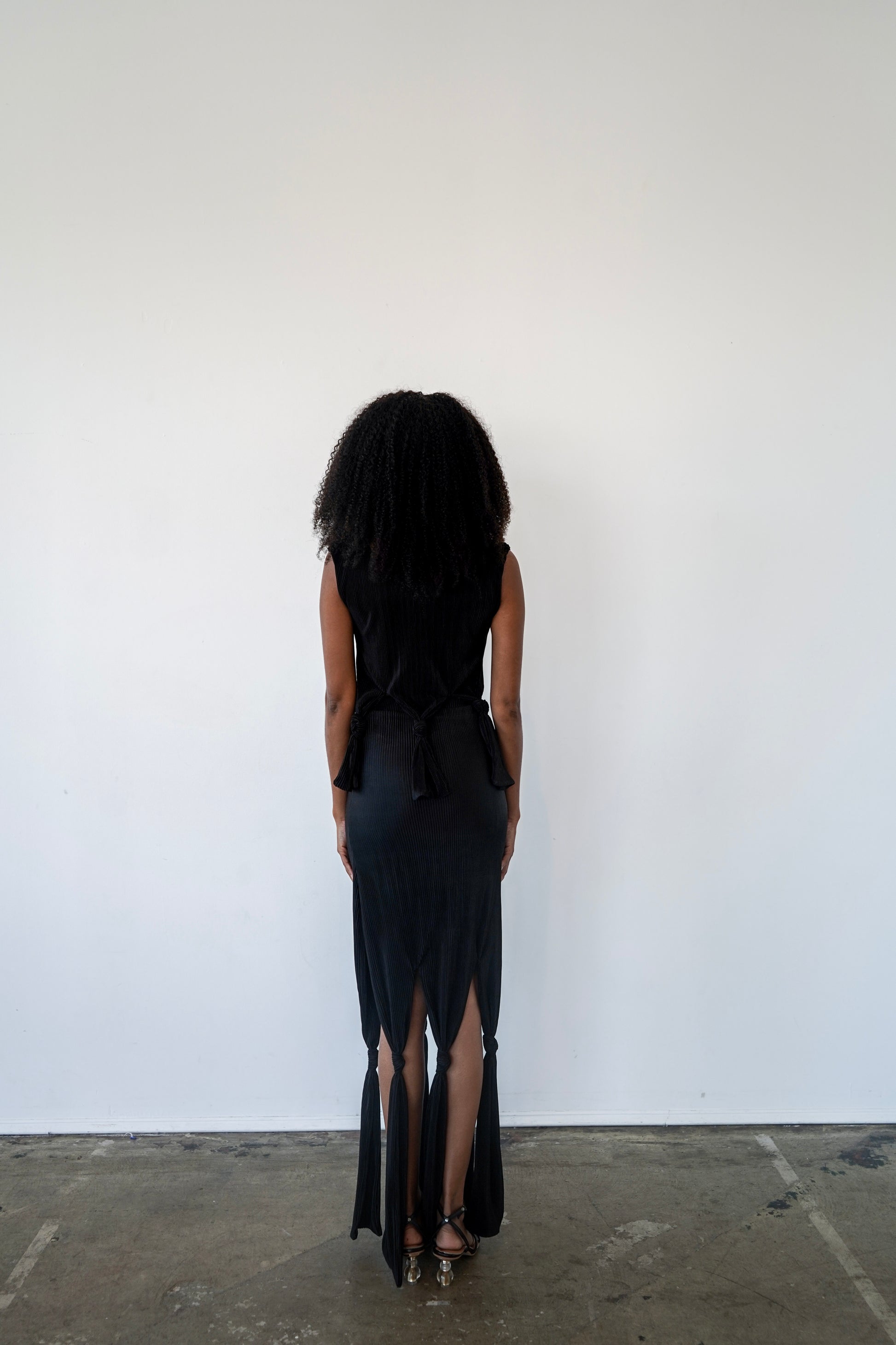 Back view of Robin Top in black – open-back design with soft plissé pleating and structured boat neckline